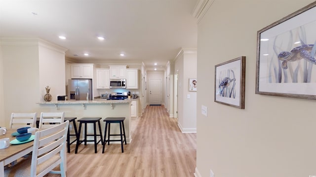 kitchen featuring white cabinets, a kitchen breakfast bar, stainless steel appliances, crown molding, and light stone countertops