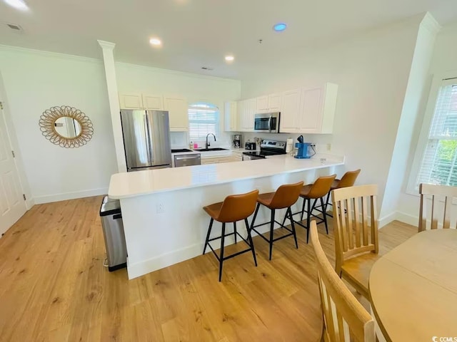 kitchen featuring appliances with stainless steel finishes, white cabinetry, sink, ornamental molding, and kitchen peninsula