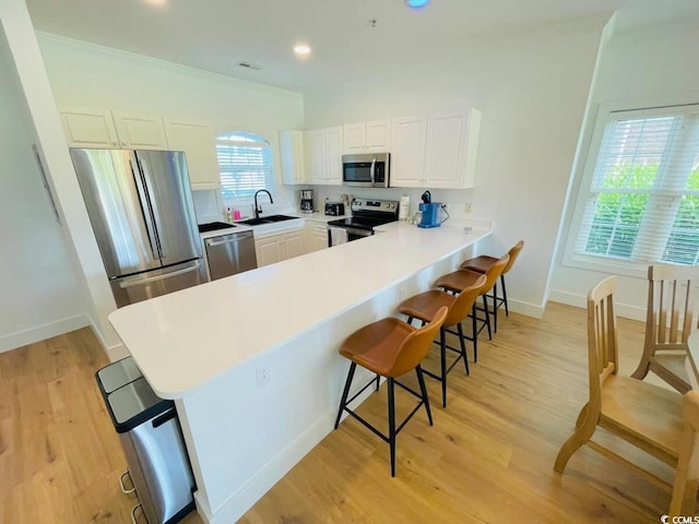 kitchen with kitchen peninsula, a kitchen bar, sink, stainless steel appliances, and white cabinets