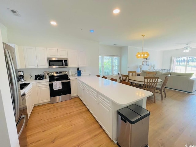 kitchen with pendant lighting, kitchen peninsula, a wealth of natural light, white cabinetry, and stainless steel appliances