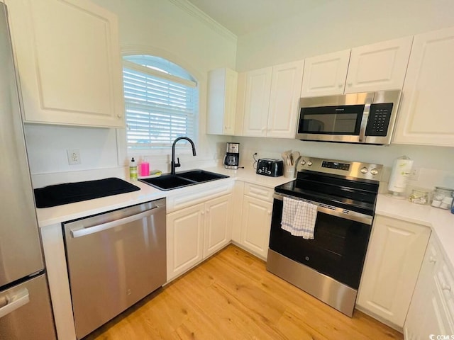 kitchen featuring appliances with stainless steel finishes, white cabinets, crown molding, light hardwood / wood-style flooring, and sink