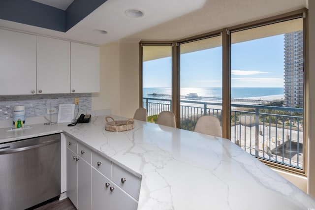 kitchen with white cabinetry, decorative backsplash, stainless steel dishwasher, a water view, and light stone countertops