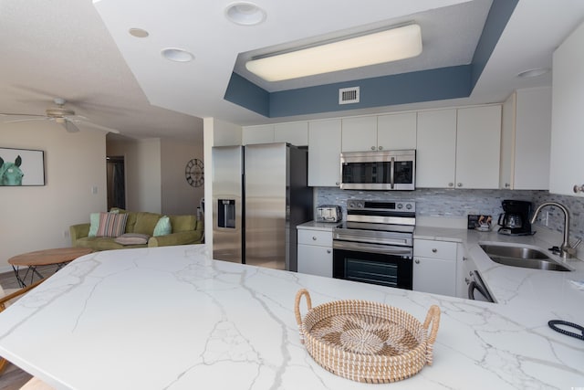 kitchen featuring sink, appliances with stainless steel finishes, kitchen peninsula, white cabinets, and backsplash