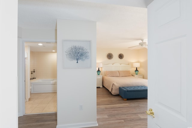 bedroom with ceiling fan, ensuite bath, and light hardwood / wood-style flooring