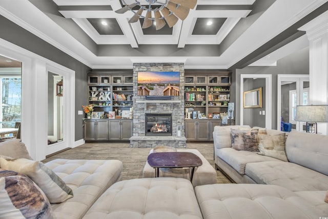 living room featuring a stone fireplace, coffered ceiling, ceiling fan, beam ceiling, and light hardwood / wood-style flooring