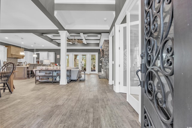 foyer featuring ornate columns, beamed ceiling, coffered ceiling, light wood-type flooring, and french doors