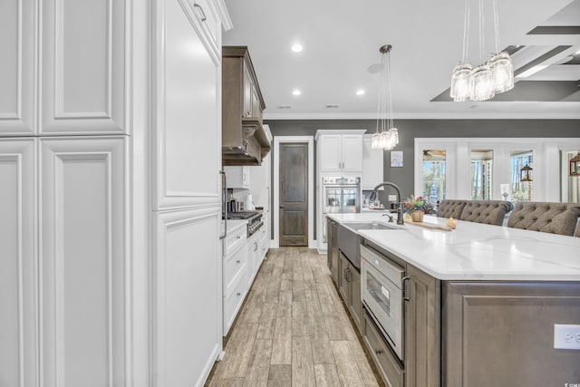 kitchen featuring sink, pendant lighting, light stone countertops, light hardwood / wood-style floors, and white cabinets