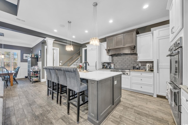 kitchen featuring stainless steel gas stovetop, an island with sink, white cabinets, a kitchen breakfast bar, and hanging light fixtures