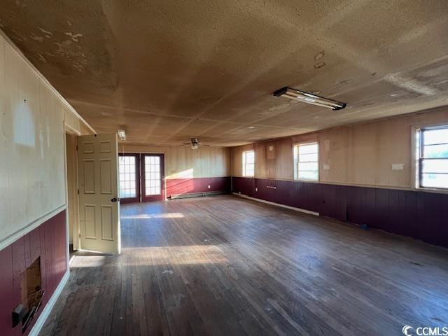 spare room with dark wood-type flooring, wooden walls, and ceiling fan