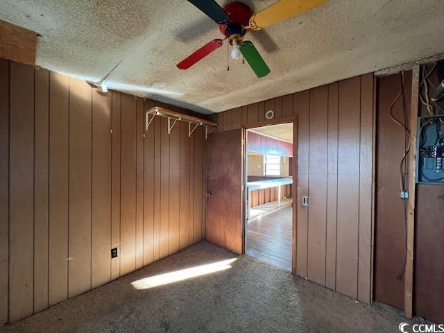 carpeted spare room with ceiling fan, a textured ceiling, and wooden walls