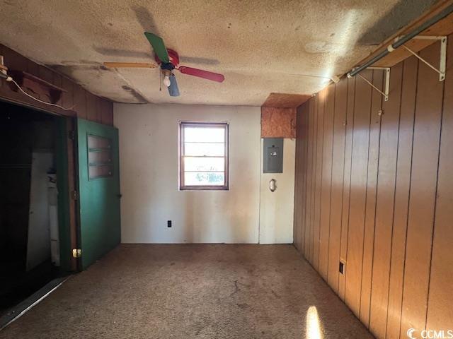 empty room featuring a textured ceiling, carpet, wood walls, ceiling fan, and electric panel