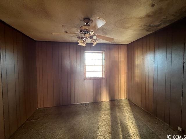 carpeted spare room featuring a textured ceiling, ceiling fan, and wood walls