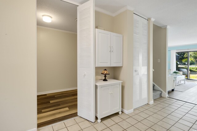 hall with light tile patterned floors, ornamental molding, and a textured ceiling