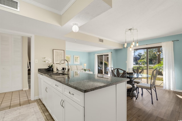 kitchen with dark stone countertops, ornamental molding, pendant lighting, white cabinets, and sink