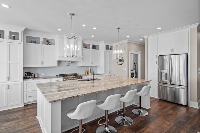 kitchen featuring stainless steel refrigerator with ice dispenser, decorative light fixtures, a kitchen island with sink, light stone counters, and sink