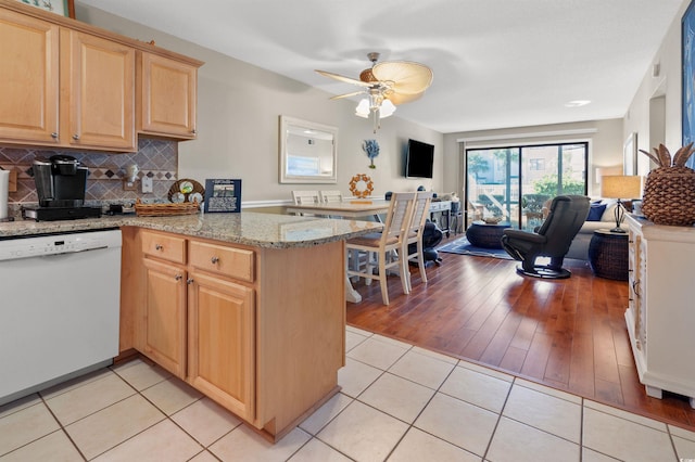 kitchen with tasteful backsplash, light stone counters, light tile patterned floors, dishwasher, and kitchen peninsula