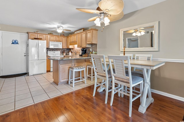 kitchen featuring light brown cabinets, dark stone countertops, kitchen peninsula, white appliances, and backsplash