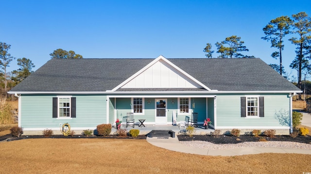 view of front of home with a shingled roof, a front lawn, a porch, and board and batten siding