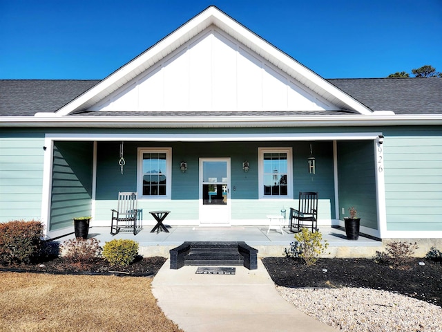 entrance to property featuring covered porch, roof with shingles, and board and batten siding