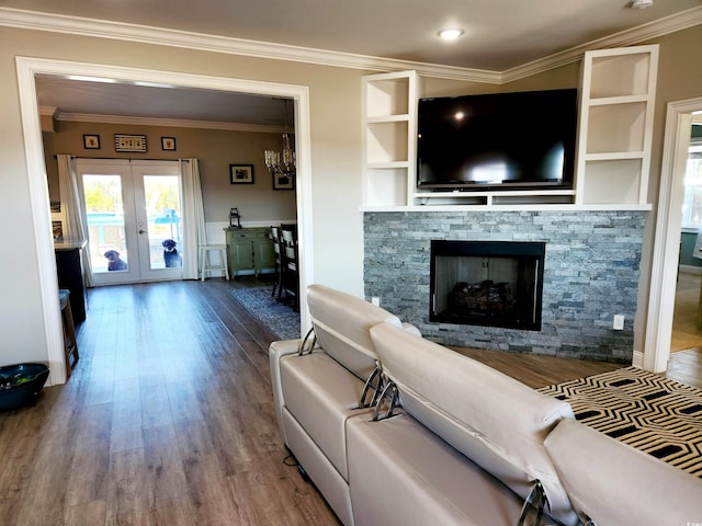 living area featuring built in features, french doors, crown molding, a stone fireplace, and wood finished floors