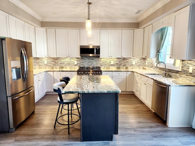 kitchen with a center island, crown molding, appliances with stainless steel finishes, a sink, and a kitchen breakfast bar