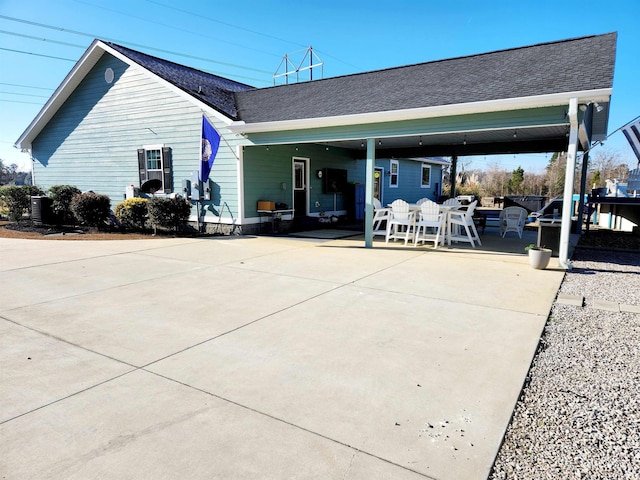 rear view of property with a shingled roof, an attached carport, and driveway