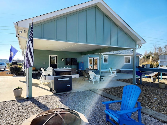 rear view of property featuring a fire pit, a patio, french doors, and board and batten siding