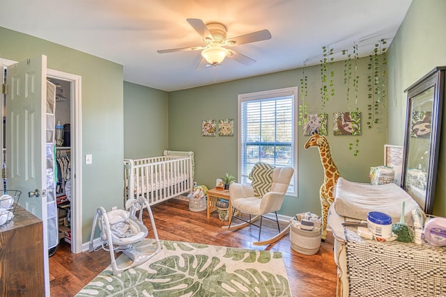 bedroom featuring ceiling fan, hardwood / wood-style flooring, and a crib