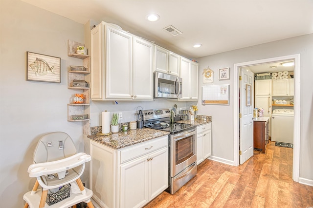 kitchen with washer / clothes dryer, white cabinetry, light wood-type flooring, appliances with stainless steel finishes, and dark stone counters