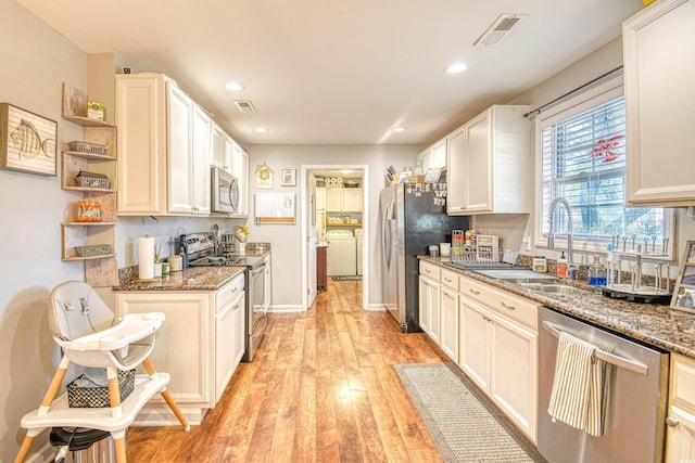 kitchen with appliances with stainless steel finishes, dark stone countertops, light hardwood / wood-style floors, and sink