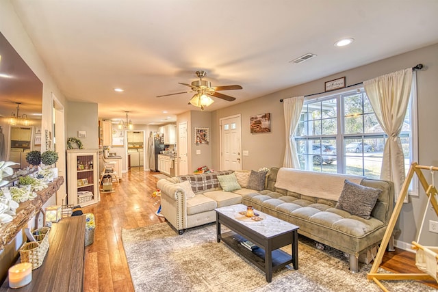 living room with light wood-type flooring and ceiling fan with notable chandelier