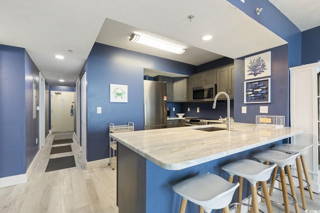 kitchen featuring light hardwood / wood-style floors, appliances with stainless steel finishes, a textured ceiling, a breakfast bar, and sink