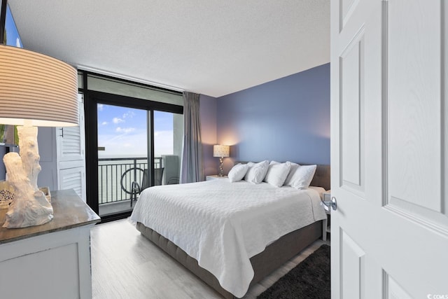 bedroom with a textured ceiling, a wall of windows, light hardwood / wood-style flooring, and access to outside