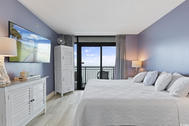 bedroom with access to outside, light hardwood / wood-style flooring, expansive windows, a textured ceiling, and a water view