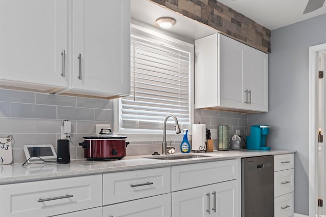 kitchen featuring stainless steel dishwasher, white cabinets, sink, and tasteful backsplash