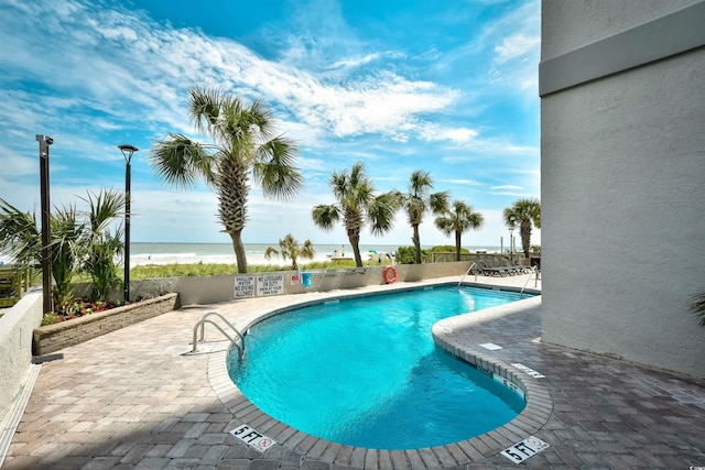 view of swimming pool featuring a beach view, a patio area, and a water view