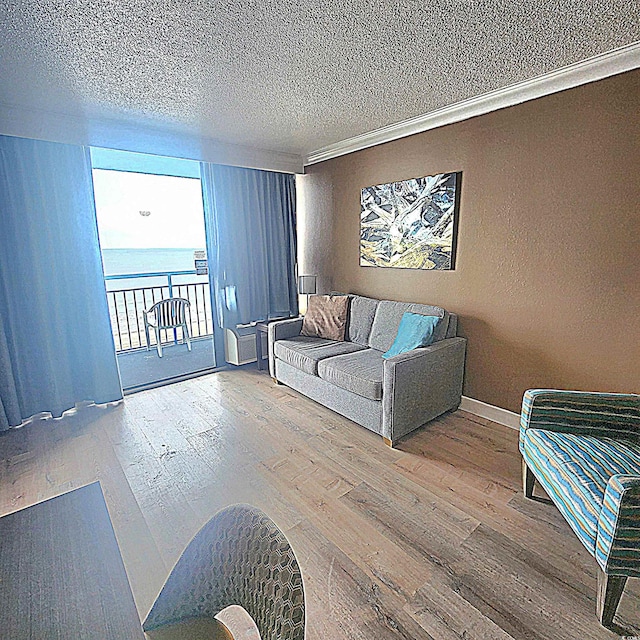 living area featuring a textured ceiling, a water view, wood finished floors, and crown molding