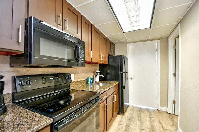 kitchen featuring a drop ceiling, dark stone countertops, black appliances, sink, and light wood-type flooring