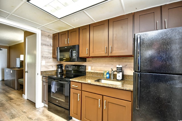 kitchen with brown cabinets, tasteful backsplash, a sink, light stone countertops, and black appliances