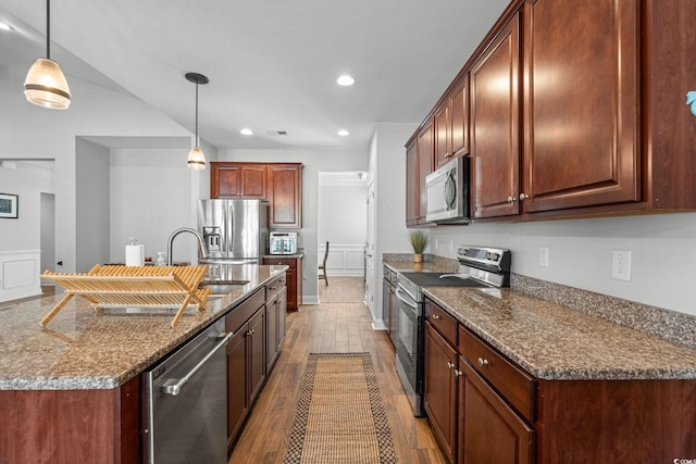 kitchen with decorative light fixtures, sink, dark stone countertops, light hardwood / wood-style floors, and stainless steel appliances