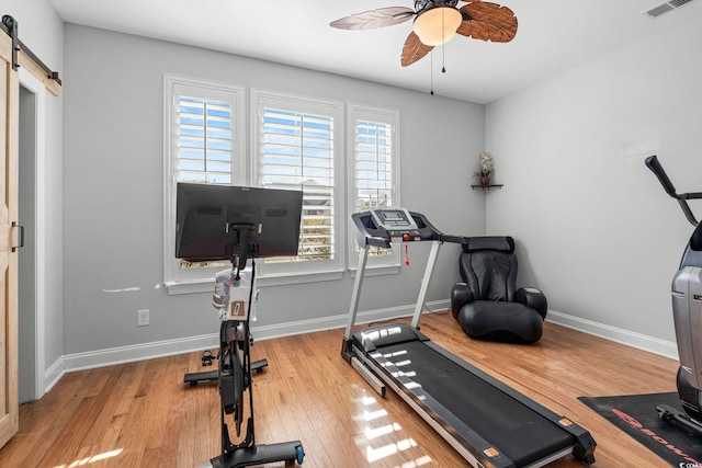 workout area with ceiling fan, a barn door, and light wood-type flooring