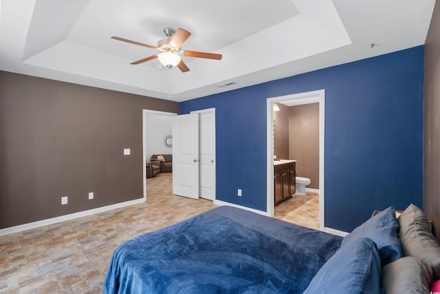 bedroom featuring a tray ceiling, ensuite bath, and ceiling fan