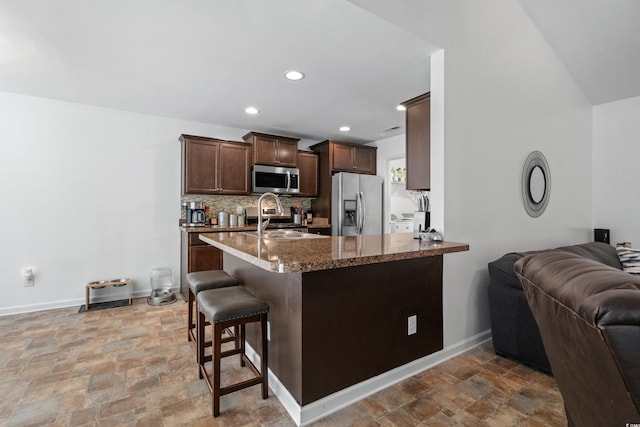 kitchen featuring a kitchen bar, sink, appliances with stainless steel finishes, kitchen peninsula, and backsplash