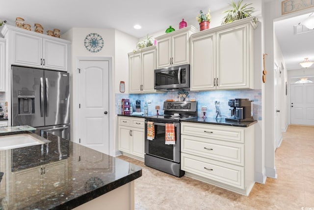 kitchen featuring white cabinetry, stainless steel appliances, tasteful backsplash, light tile patterned flooring, and dark stone countertops