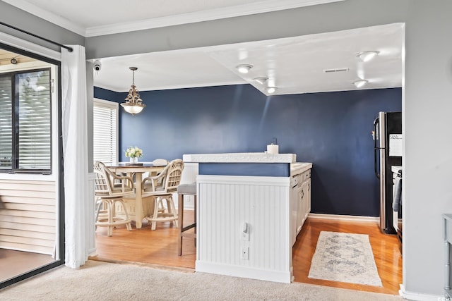 kitchen featuring hanging light fixtures, white cabinets, stainless steel fridge, and ornamental molding