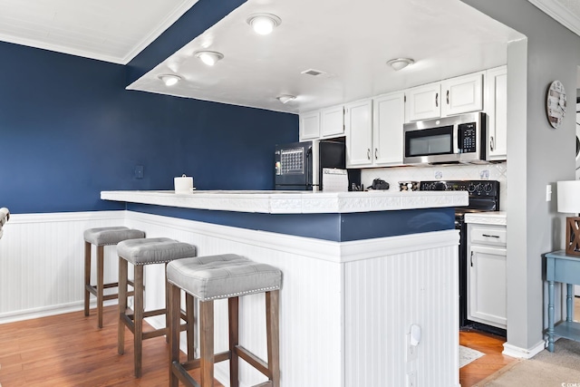 kitchen featuring white cabinets, appliances with stainless steel finishes, a kitchen breakfast bar, ornamental molding, and light wood-type flooring