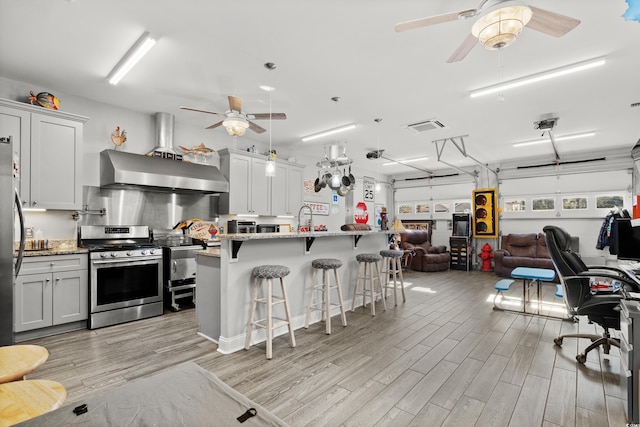 kitchen featuring stone countertops, wall chimney range hood, a breakfast bar, and appliances with stainless steel finishes