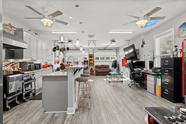 kitchen with pendant lighting, white cabinetry, light stone counters, a kitchen bar, and light wood-type flooring