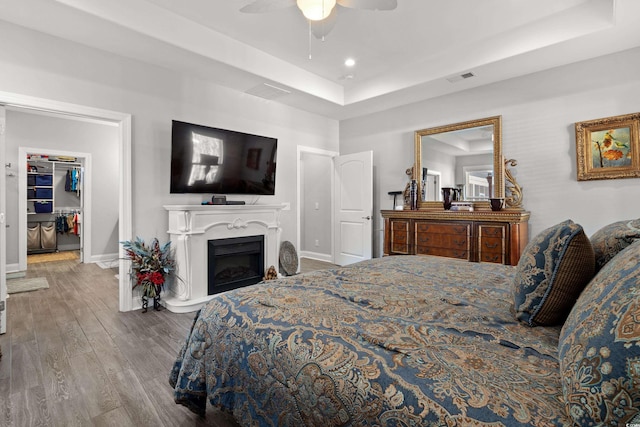 bedroom with a tray ceiling, a spacious closet, ceiling fan, and hardwood / wood-style flooring