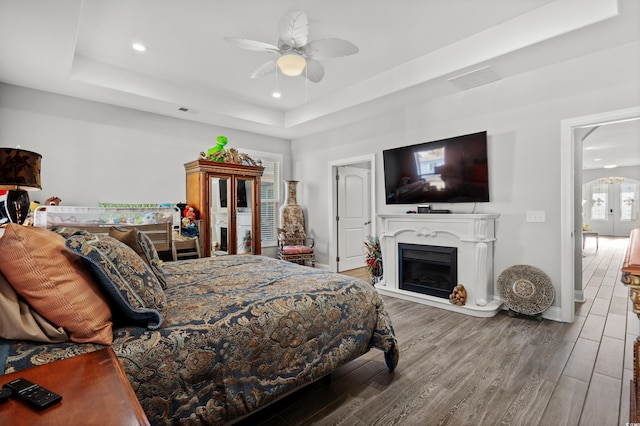 bedroom with wood-type flooring, ceiling fan, and a tray ceiling